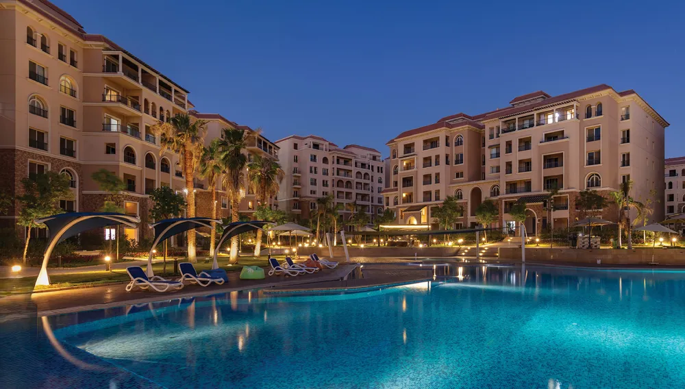 Evening view of a lit pool beside terracotta apartment buildings - apartment in Serenity 90 Avenue, New Cairo