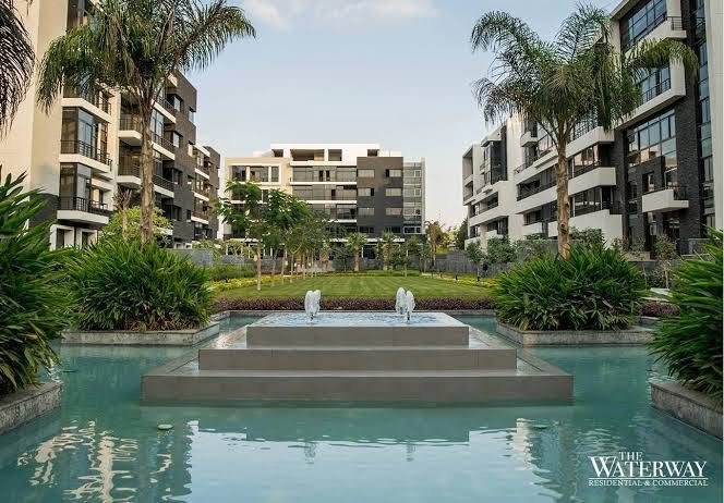 Fountain pool surrounded by palm trees and apartment buildings - apartment in The View by Waterway, New Cairo