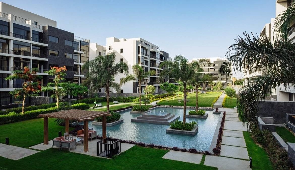 Garden with a pergola, pond and paved paths between apartment blocks - apartment in The View by Waterway, New Cairo