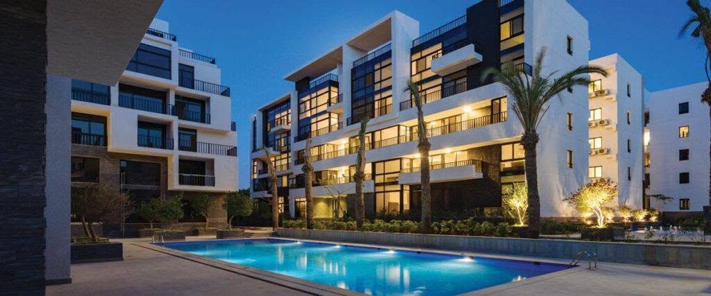 Apartment buildings and a lit pool at dusk - apartment in The View by Waterway, New Cairo