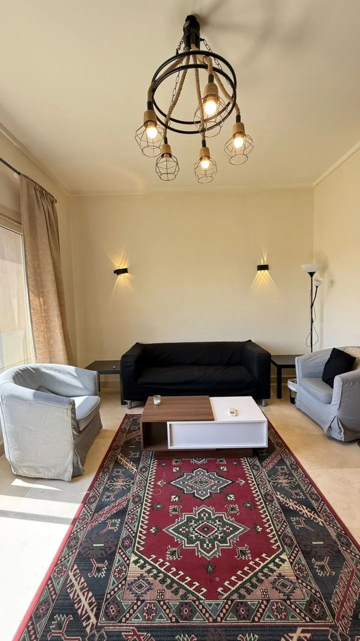 Seating area with a red Persian rug, a black sofa and a woven pendant - villa in The Village, 5th Settlement