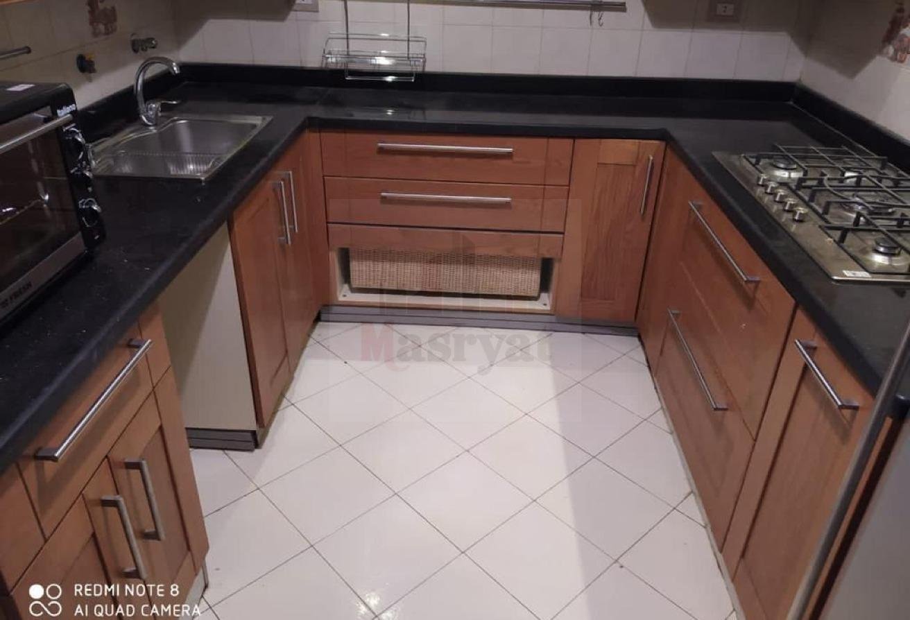 third-district-apt-135-06 U-shaped kitchen with black counters and white floor tiles - apartment in 3rd District, New Cairo