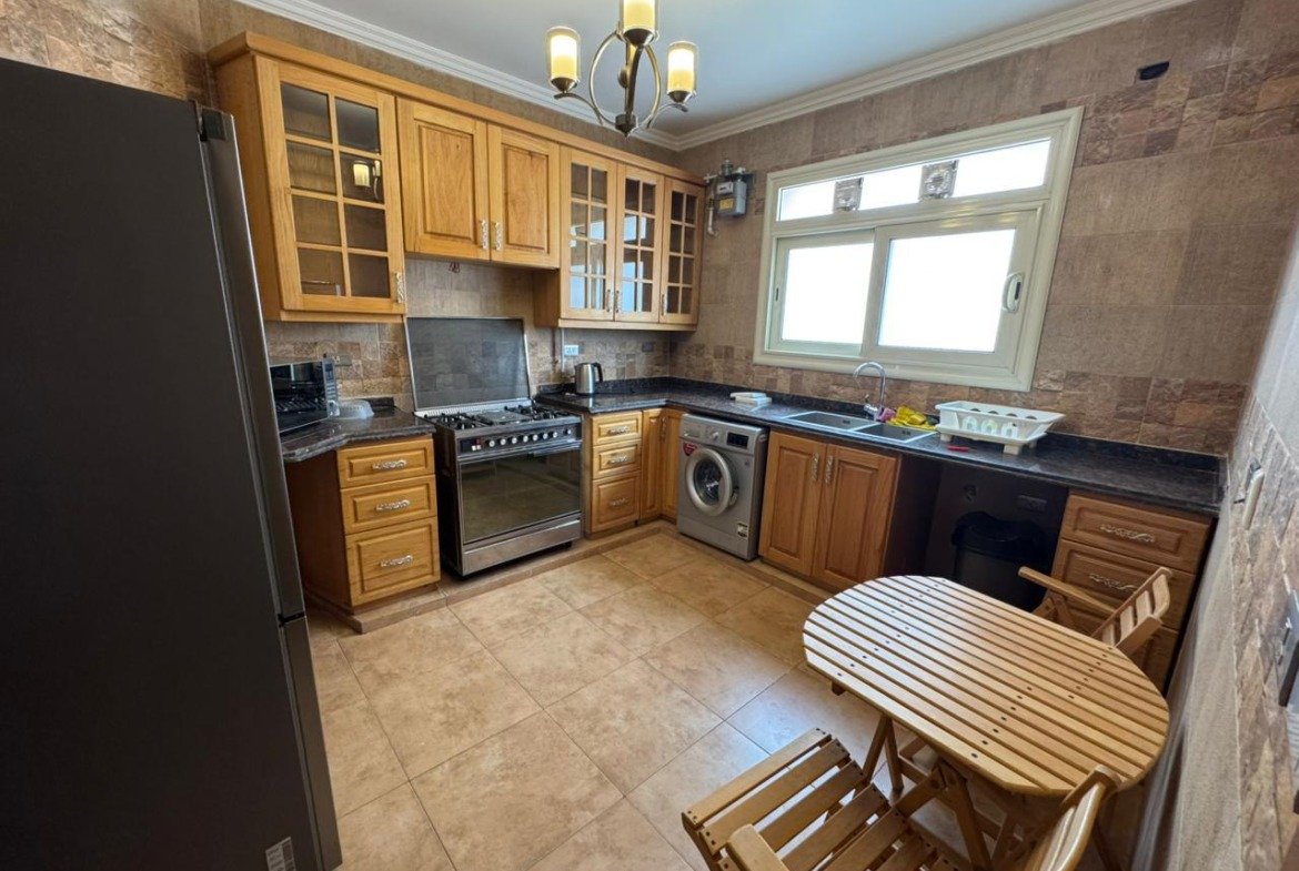 Kitchen with a round wooden table and a washing machine - apartment in El Yasmeen 4, New Cairo